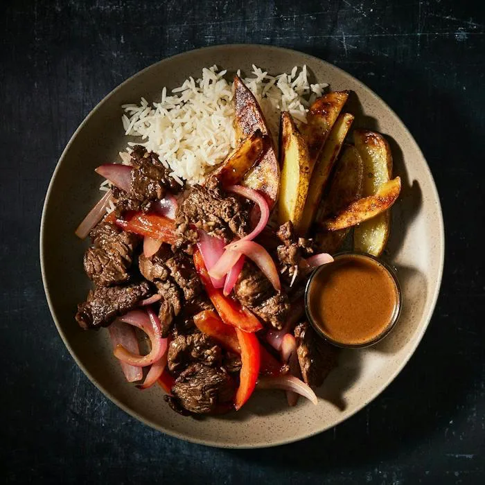A CookUnity beef stir-fry with peppers and onions, served with rice and potato wedges.
